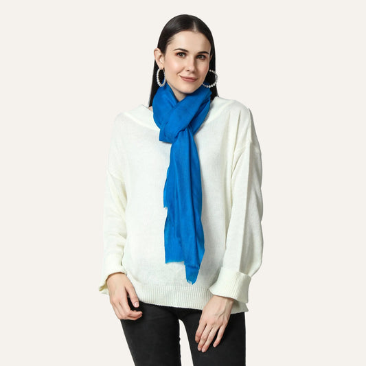 A woman wearing a blue cashmere scarf with a white top and black pants.