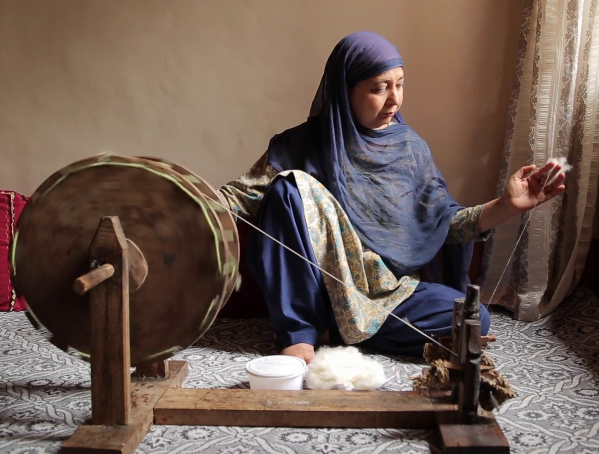 An Kashmiri woman sitting behind a wheel and is hand spinning the raw cashmere fibres into a yarn 
