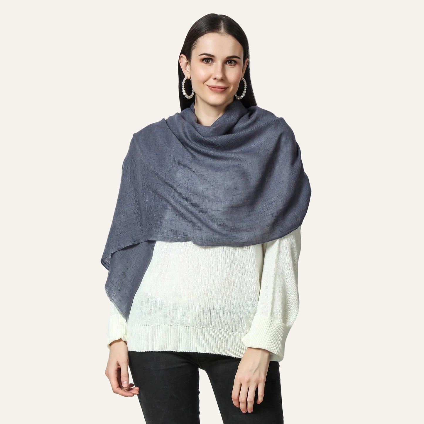 A woman wearing a gray cashmere scarf and a white sweater with black trousers.