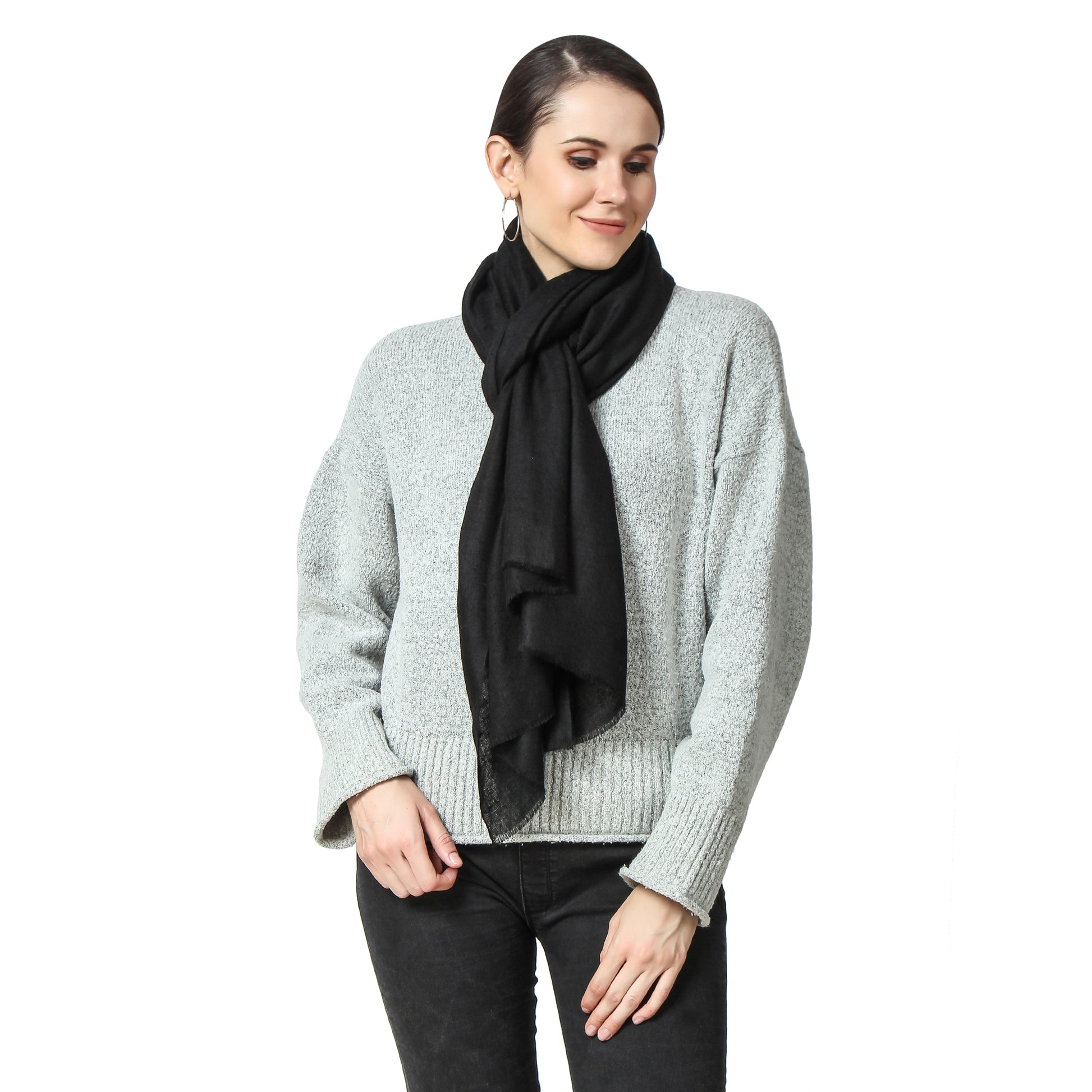 Image of a woman wearing a black cashmere scarf around her neck, knotted in a stylish and elegant way. The knot is positioned off-center and adds a touch of sophistication to the woman's outfit. The woman's expression is confident and composed, with a subtle smile on her face.