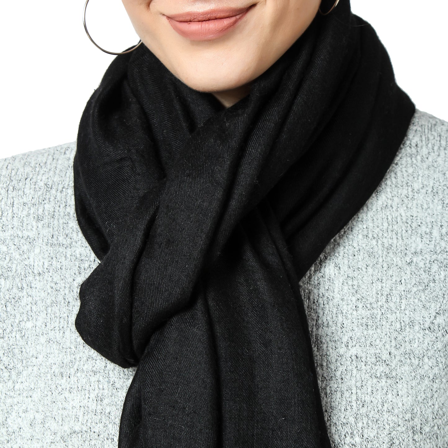 Close-up image of a black cashmere scarf knotted around a woman's neck. The knot is positioned in the center, and the ends of the scarf are neatly tucked in. The soft and luxurious texture of the scarf is visible, and the black color adds to its elegance and versatility. The image focuses on the knot and the way the scarf drapes around the woman's neck, adding a touch of sophistication to her outfit.