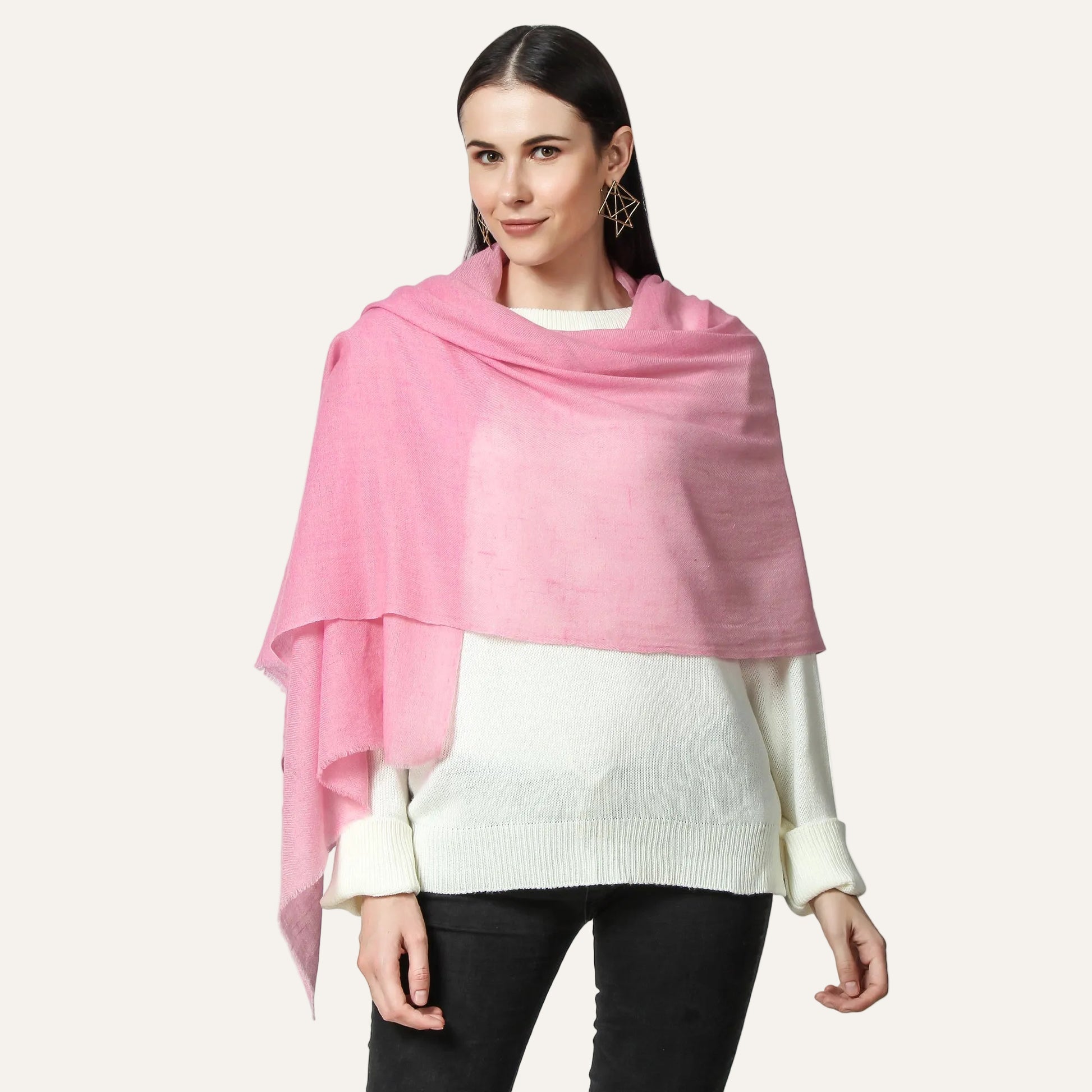 A woman wearing a pink cashmere scarf with a white sweater and black pants.