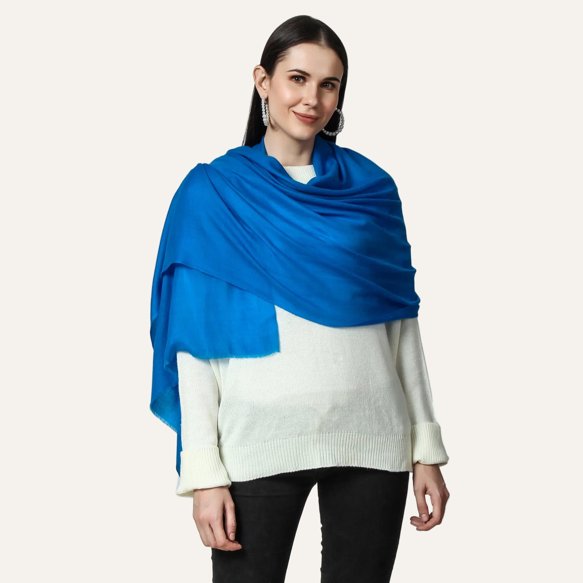 A woman wearing a blue cashmere scarf wrapped around her shoulders, paired with a white top and black pants.