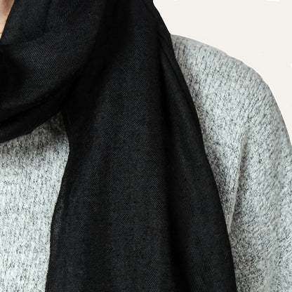 Close-up image of a black cashmere scarf, showing the intricate details of its soft and luxurious texture. The scarf appears to be made with high-quality material, and the black color adds to its classic and timeless style. The image focuses on the texture and appearance of the scarf, with no other elements in the frame.