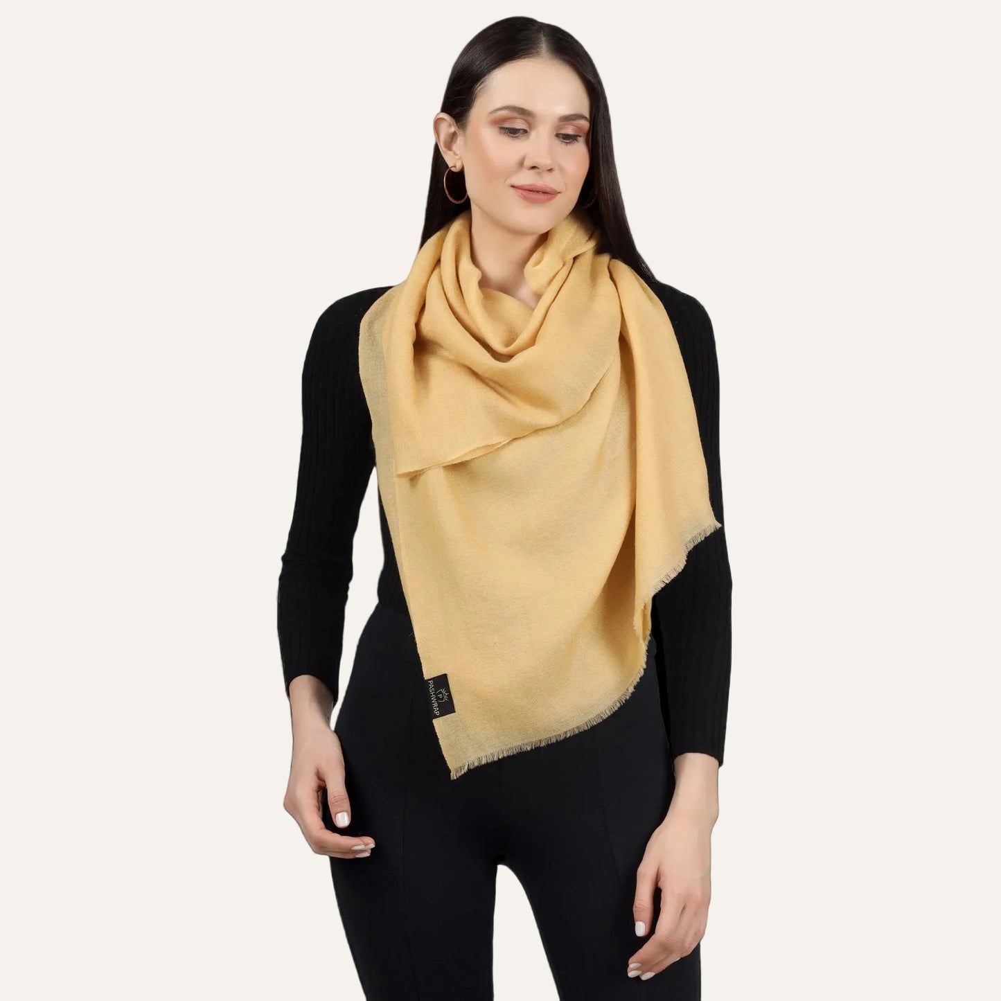 A woman wearing a golden cashmere scarf as a wrap, draped over the shoulders.