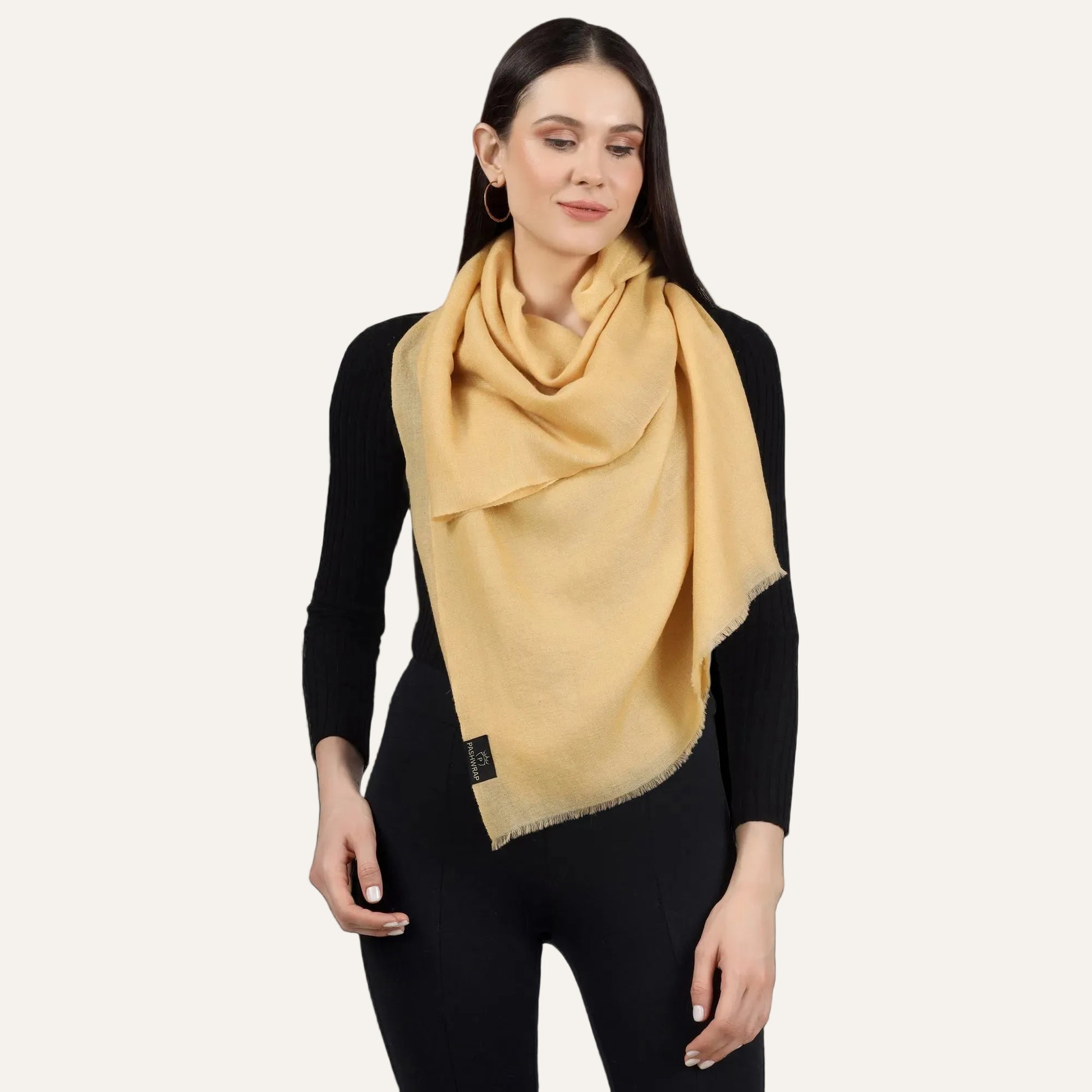 A woman wearing a golden cashmere scarf as a wrap, draped over the shoulders.